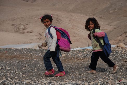 To smilende børn går på grusvej med rygsæk i Israel Palæstina