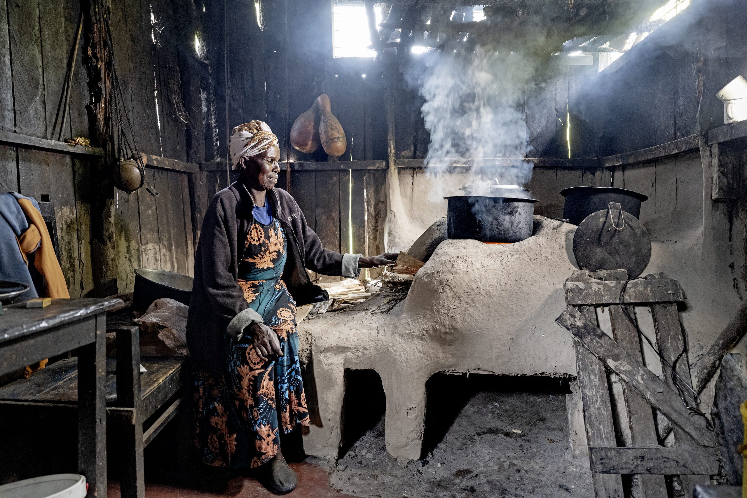 Kvinde sidder ved sit traditionelle komfur med røg over det hele - Folkekirkens Nødhjælp