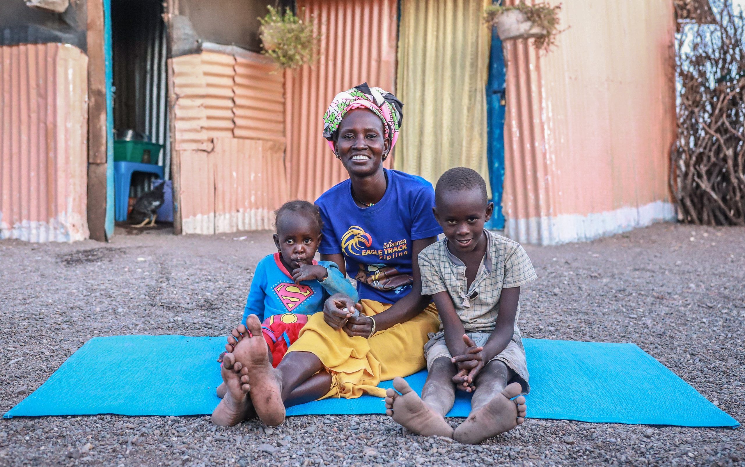 Emily sitting on a blue mat with her two children by her side smiling at the camera.