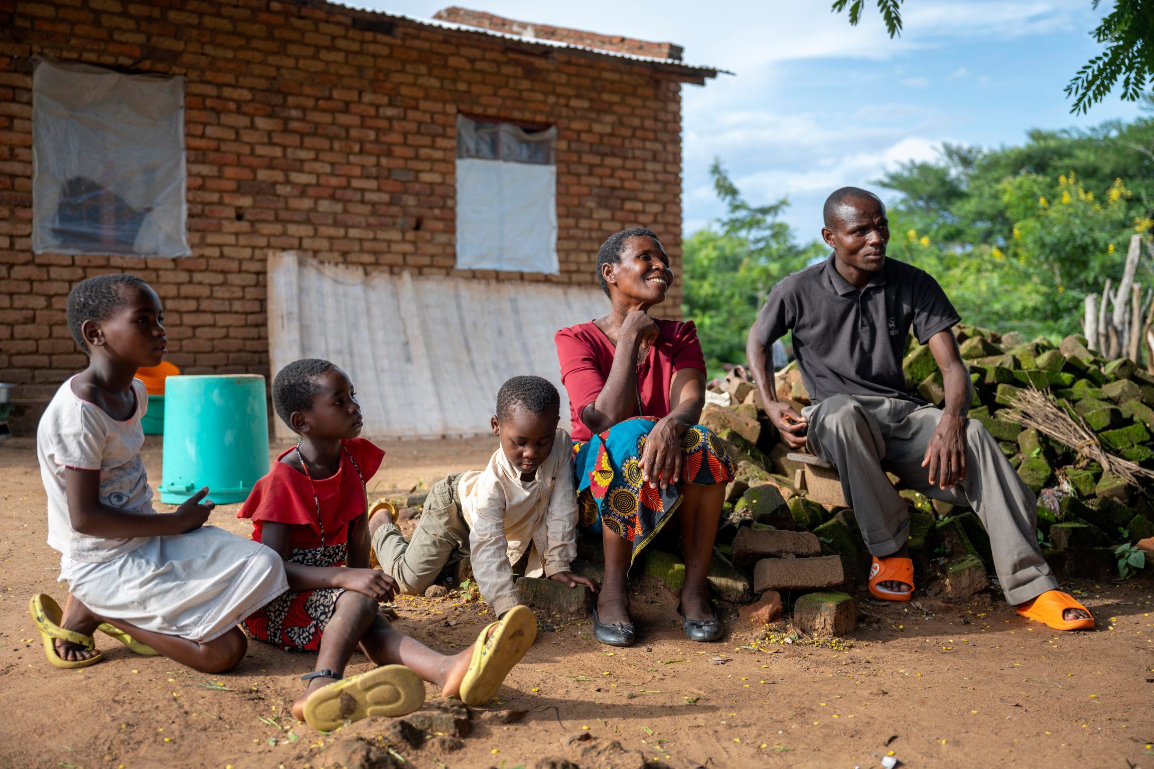 Jessie Kumwenda (midten) sidder sammen med hendes søn (højre) og sit barnebarn, som leger med naboens børn.