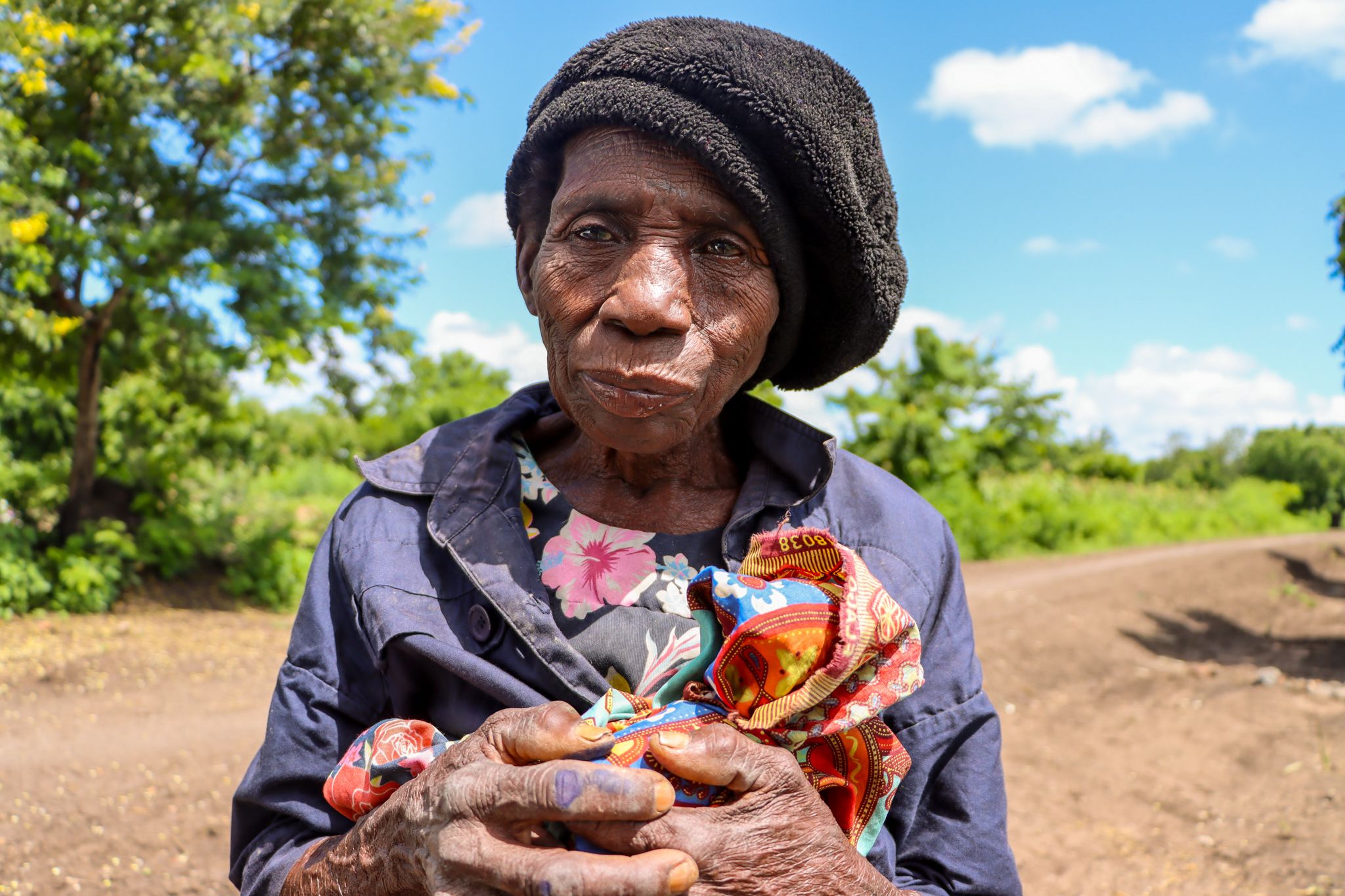 Ældre dame fra Malawi står med hendes sidste stykker tøj i armene.