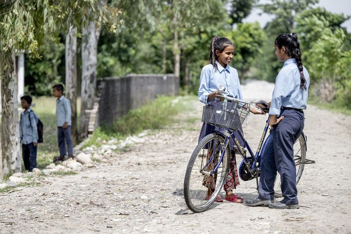 To skoleelever står ved en cykel og smiler til hinanden