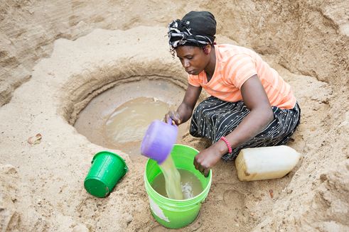 Kvinde arbejder ved et vandhul og skovler vand op