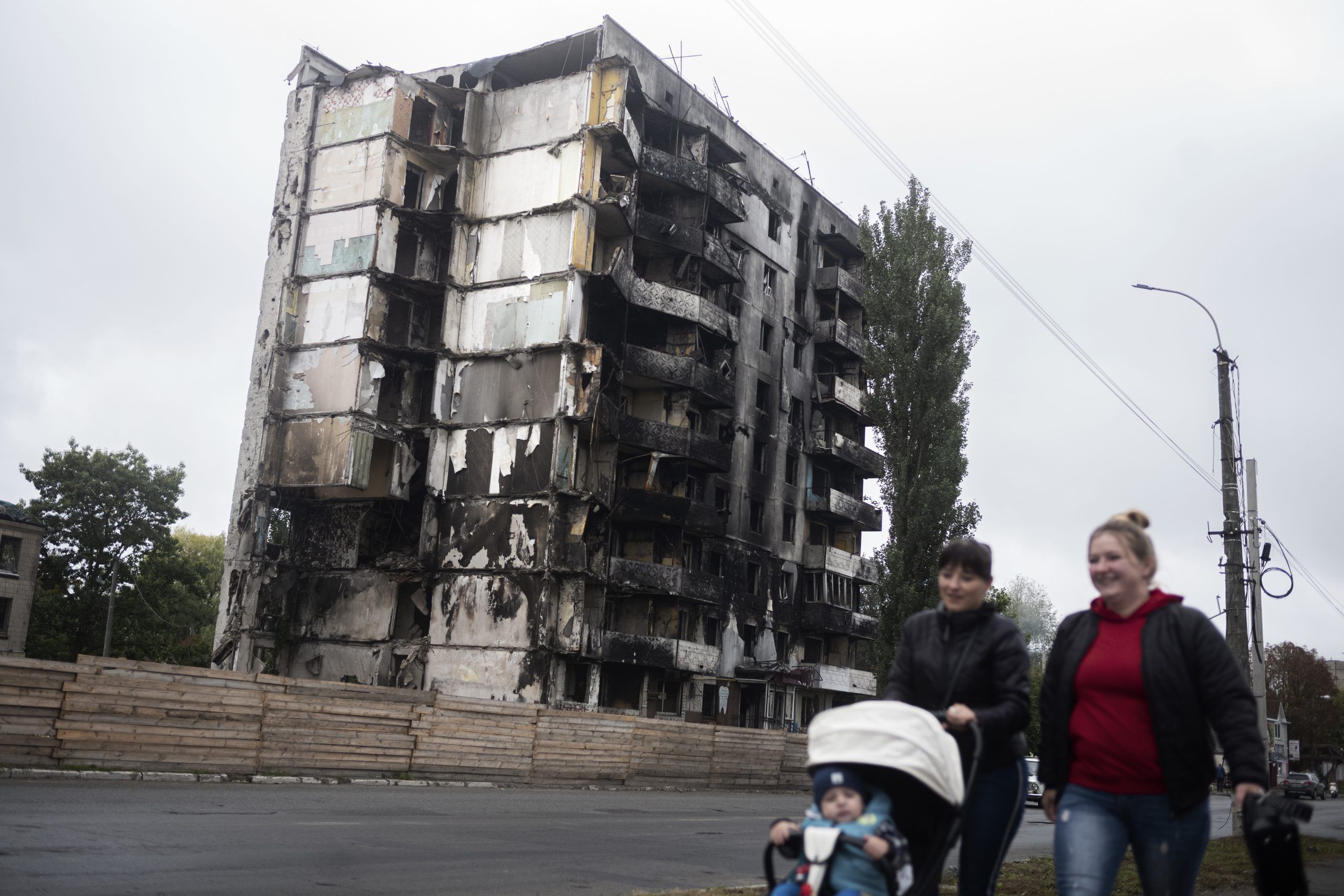 To kvinder og en baby foran bombarderet bygning. Bucha, Ukraine