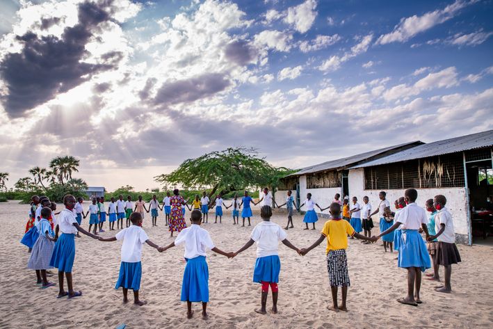 Kenyanske børn i skoleuniform står i rundkreds med hinanden i hånden - Folkekirkens Nødhjælp