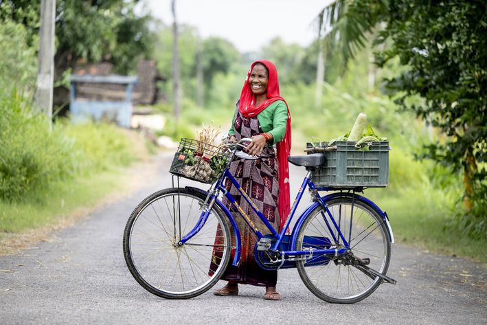 Kvinde står med cykel fyldt med grønsager i cykles kurve