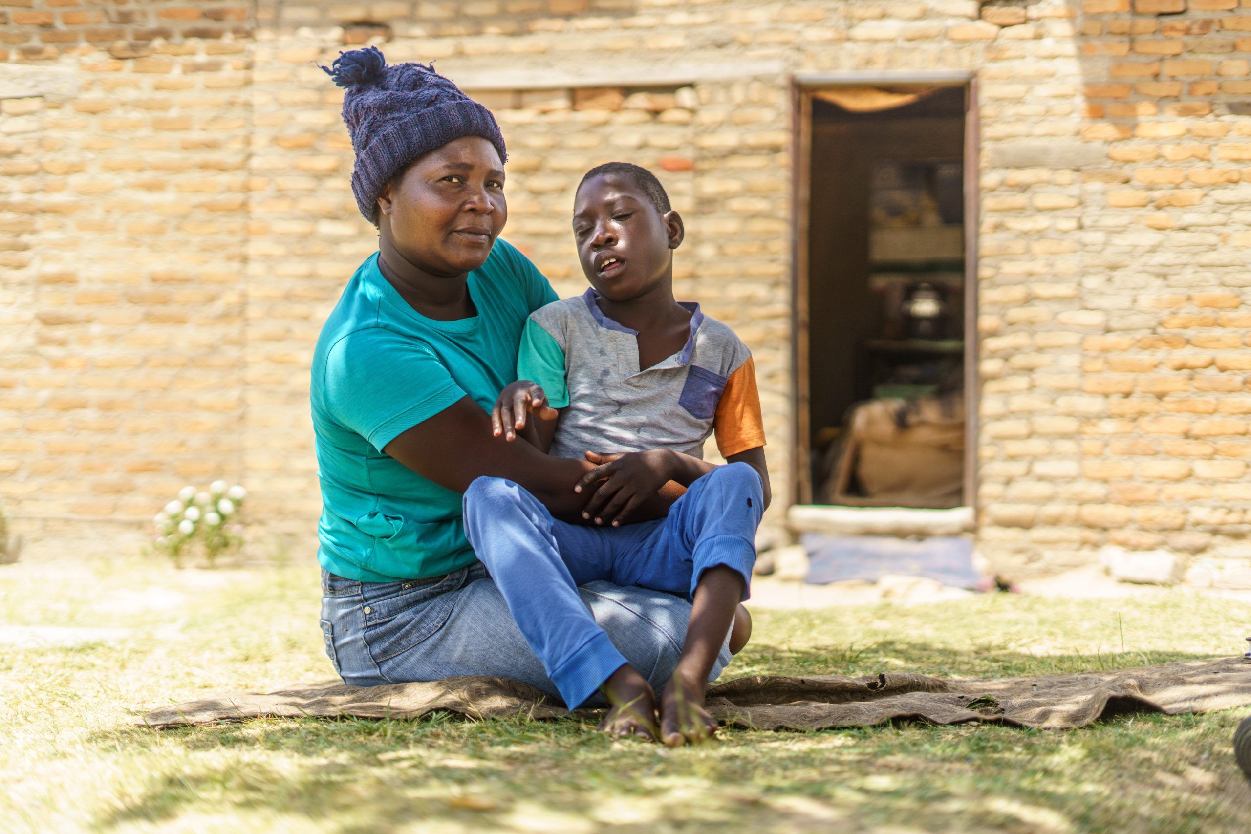 Christine Amos sidder med sin handicappede 9-årige søn uden for sit hus i Harare, Zimbabwe.