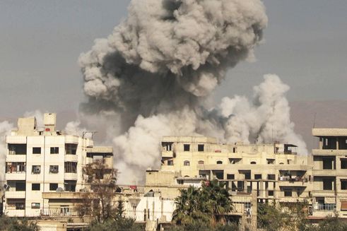 Grå røg stiger til vejrs bag bygninger ramt af bomber i Syrien